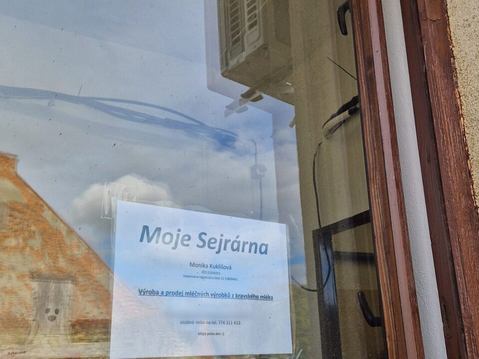 Výdejní okénko sýrárny zvenku s cedulí Moje Sejrárna v okně